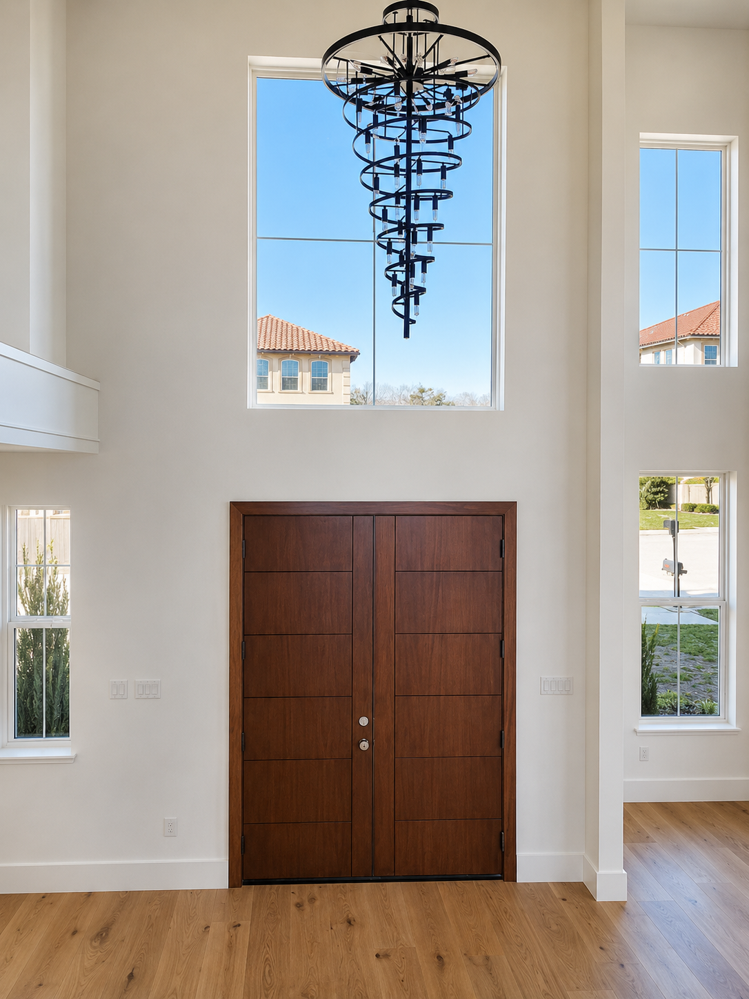 Custom home entry with tall chandelier, warm wood door, and bright interior finishes