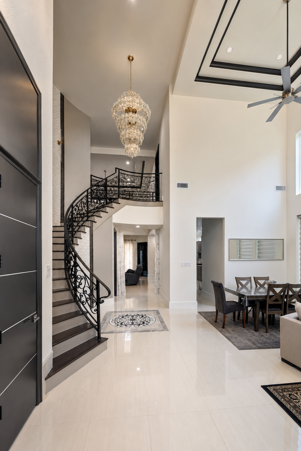 Contemporary Mediterranean home entry with curved black iron staircase, chandelier, and dining area