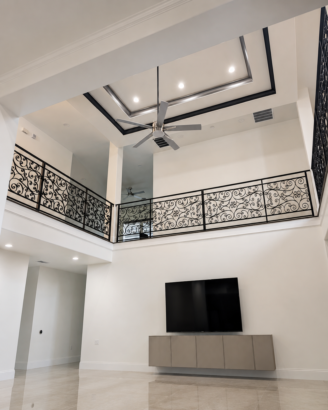 Double-height living room with black wrought-iron balcony railing and recessed ceiling detail